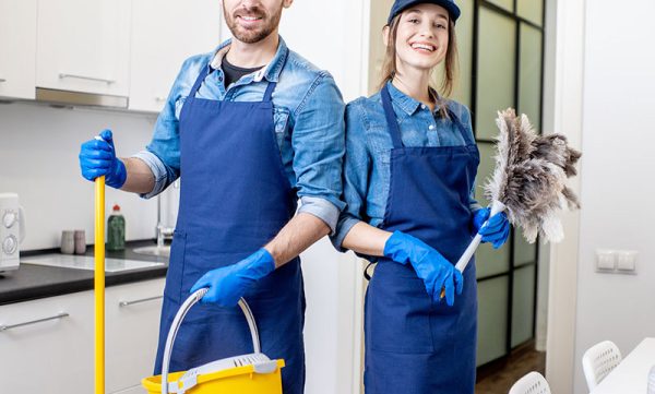 Portrait of a couple as a professional cleaners in uniform standing together with cleaning tools indoors